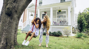 Happy mother pushing daughter on swing in front yard at home